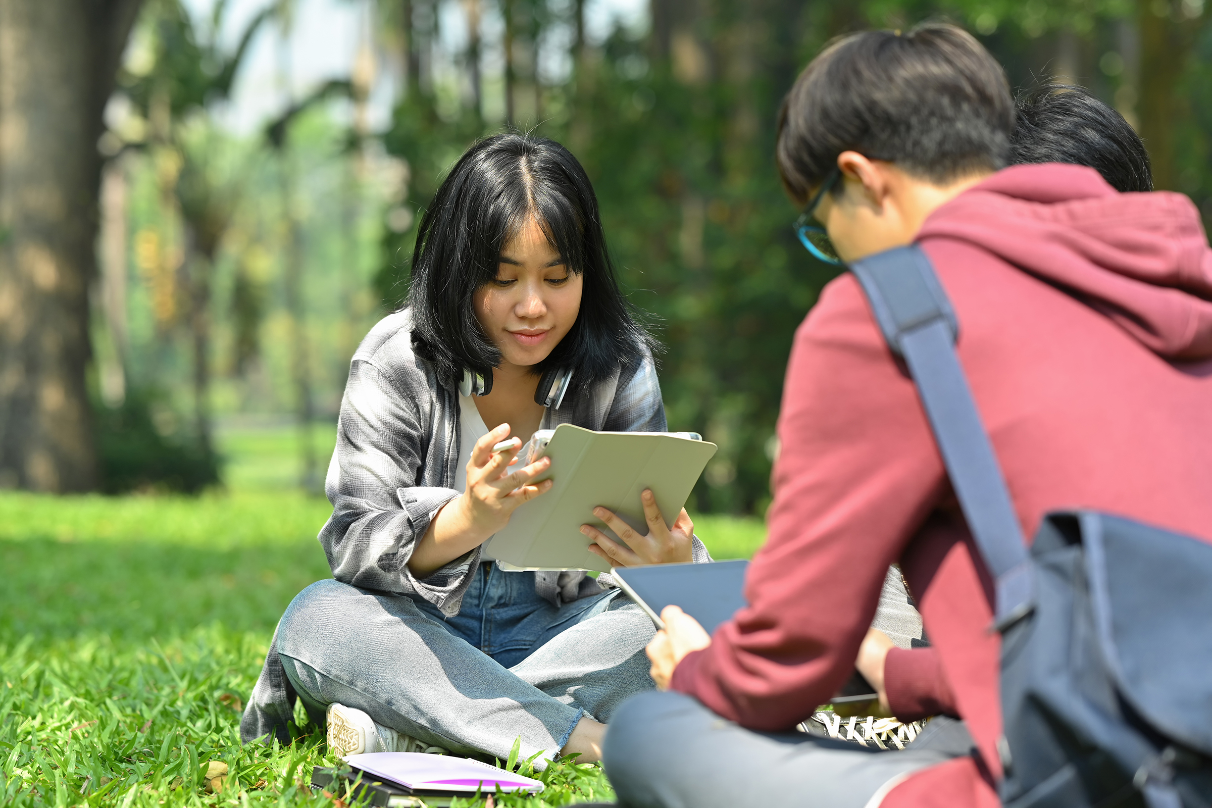 Image of asian female student reading books with her friends at summer park. Education and lifestyle concept.