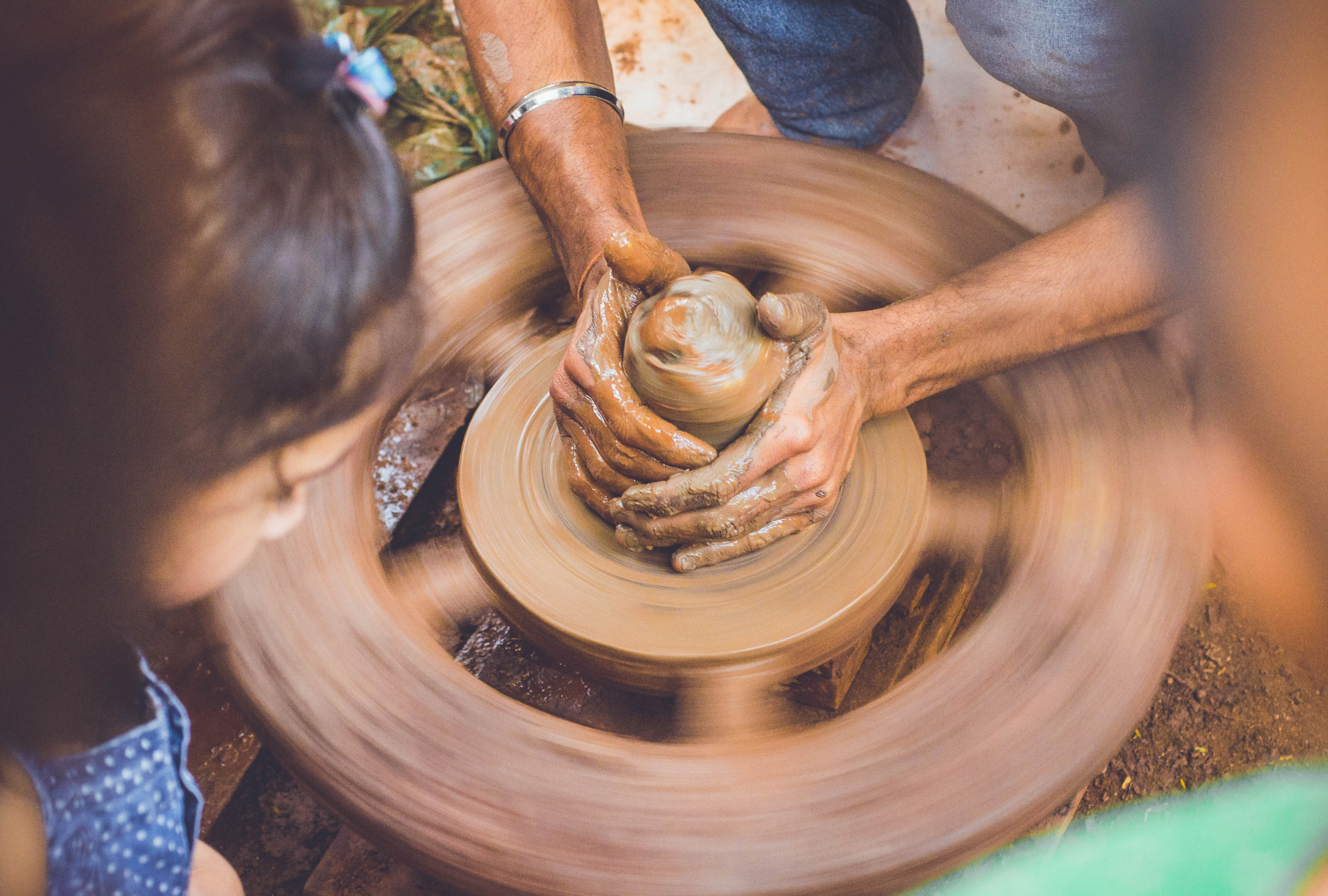 Hands crafting clay while a little girl watches