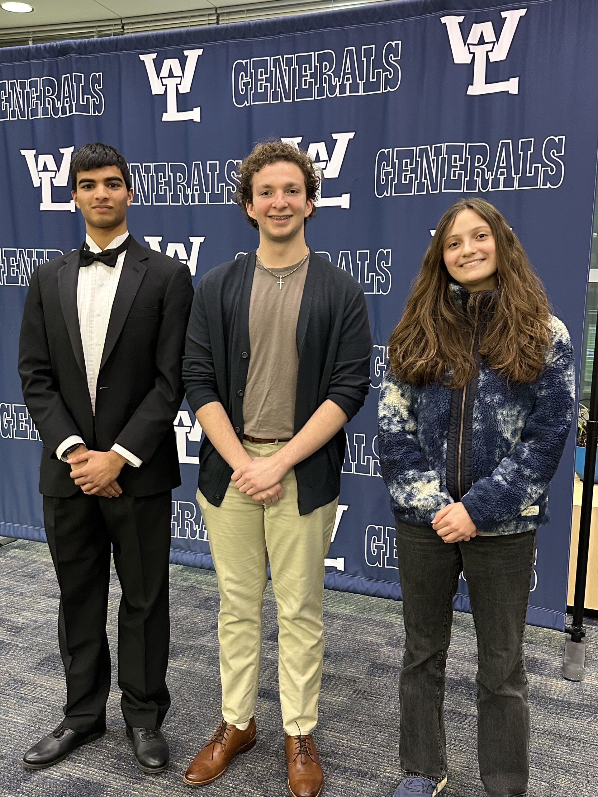 Arjun Rao, Sebastian Berisha, Natalie Faust, in front of W-L banner